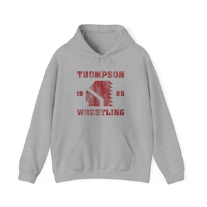 May include: A gray hooded sweatshirt with a red vintage-style graphic that says "Thompson Wrestling" with a sawtooth logo and the years "19 85" on either side.