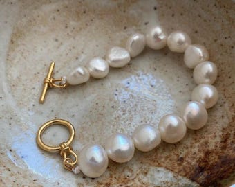 Puede incluir: Un brazalete de oro con cierre de palanca presenta una hebra de perlas barrocas blancas. Las perlas son de forma y tamaño irregulares, lo que le da al brazalete un toque único y natural.
