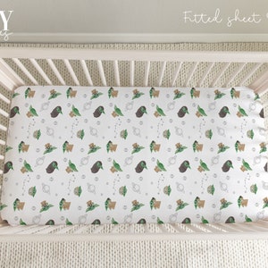 Op de afbeelding: Witte, strakke babybedlakens met een herhalend patroon van groene baby Yoda-figuren, bruine beren en planeten op een witte achtergrond. De tekst "Fitted sheet Option |" is zichtbaar in de rechterbovenhoek van de afbeelding.