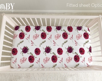 Può includere: Un lettino bianco con un lenzuolo con angoli elasticizzato con un motivo floreale di rose bordeaux e rosa su sfondo bianco. Il testo "Fitted sheet Option 1" è visibile nell'angolo in alto a destra dell'immagine.