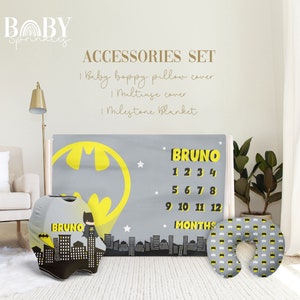 May include: A baby milestone blanket with a Batman theme. The blanket is gray with a yellow Batman symbol and stars. The blanket also has a number chart for tracking a baby's growth. The set includes a matching boppy pillow cover and a travel pillow.