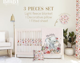 Puede incluir: Un juego de ropa de cama para cuna de bebé de 3 piezas con un diseño floral y de elefante. El juego incluye una manta de forro polar ligera, una almohada decorativa y una sábana ajustable. La manta presenta una ilustración de acuarela de un elefante con flores y el nombre "Matilda".