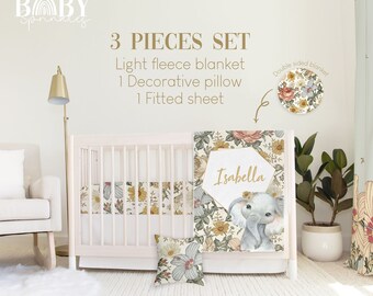 Puede incluir: Un juego de ropa de cama para cuna de bebé de 3 piezas con un diseño floral y de elefante. El juego incluye una manta de forro polar ligera, una almohada decorativa y una sábana ajustable. La manta presenta un lindo elefante con un fondo floral y el nombre "Isabella" en letras doradas. La almohada y la sábana ajustable tienen un patrón floral a juego.