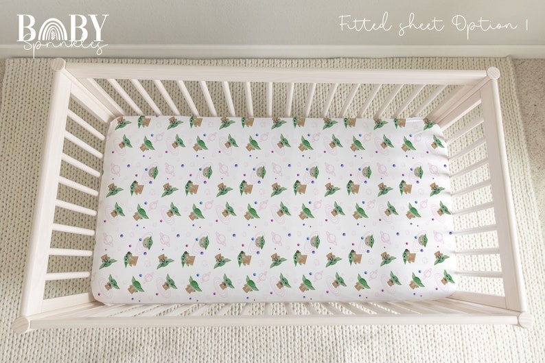 May include: A white crib with a fitted sheet featuring a repeating pattern of green and brown baby Yoda characters with pink and blue dots. The sheet is labeled "Fitted sheet Option | Baby Sprinkles".