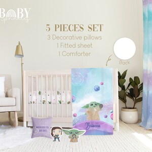 May include: A 5-piece baby bedding set featuring a watercolor design of a green alien character with planets and stars. The set includes a comforter, fitted sheet, and three decorative pillows. The comforter has the text "Brianna" on it. The pillows have the text "Wherever I go, she goes".