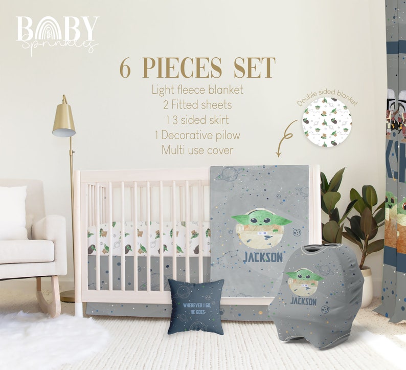 Op de afbeelding: Een 6-delige babybeddenset met een grijs en wit ruimtethema met een groen alien-personage. De set bevat een licht fleece deken, twee hoeslakens, een 3-zijdige rok, een decoratief kussen en een multifunctionele hoes. De set is gepersonaliseerd met de naam "JACKSON".
