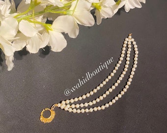 May include: A gold nose ring with three strands of white pearl beads. The nose ring is a traditional Indian jewellery piece.