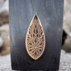 May include: A wooden pendant necklace with a teardrop-shaped design. The pendant features a detailed, intricate laser-cut pattern.
