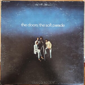 May include: Album cover for "The Doors / The Soft Parade" featuring the band members in suits and jackets. The album art has a dark blue and black gradient background with the band's name and album title in white text.