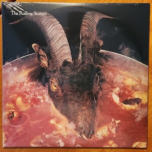 May include: The Rolling Stones album cover featuring a goat's head submerged in a red liquid with bones and other objects. The album title "The Rolling Stones" is printed in white at the top of the cover.