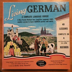 May include: A vintage box set for learning German. The box features a colorful illustration of a German castle, a cow, and two people. The text on the box reads "Living German, A Complete Language Course, 40 Lessons, Complete on 4 Records".