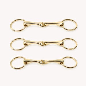 May include: Three gold-colored horse bits with round rings on each end. The bits are arranged in a vertical stack.