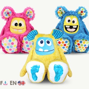 May include: Three plush toys shaped like monsters. The monsters are yellow, pink and blue. They have large eyes, toothy grins and colourful polka dots on their feet.