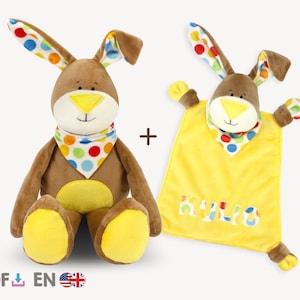May include: A brown plush bunny with yellow accents and a colorful polka dot scarf. The bunny is sitting and holding a yellow plush blanket with the word "Hello" embroidered on it.