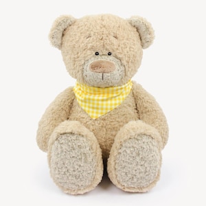 Puede incluir: Un oso de peluche con una bandana a cuadros amarillos y blancos. El oso est&aacute; sentado con las piernas cruzadas y tiene un pelaje suave y marr&oacute;n.