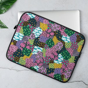May include: A laptop sleeve with a colorful patchwork design featuring pink, green, yellow, and blue geometric shapes and floral patterns.