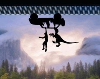 May include: A silhouette of a car being lifted by a dinosaur, with a person hanging on to the car. The scene is set against a backdrop of a misty forest and mountains.