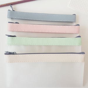 May include: Four clear zippered pouches with different coloured fabric trim. The pouches are stacked on top of each other. The top pouch has a grey trim, the second pouch has a pink trim, the third pouch has a light green trim, and the bottom pouch has a beige trim.
