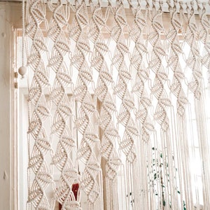 Peut inclure: Un rideau en macramé blanc avec un motif géométrique suspendu à une tringle blanche. Le rideau est fait de cordon de coton épais et a une frange en bas.