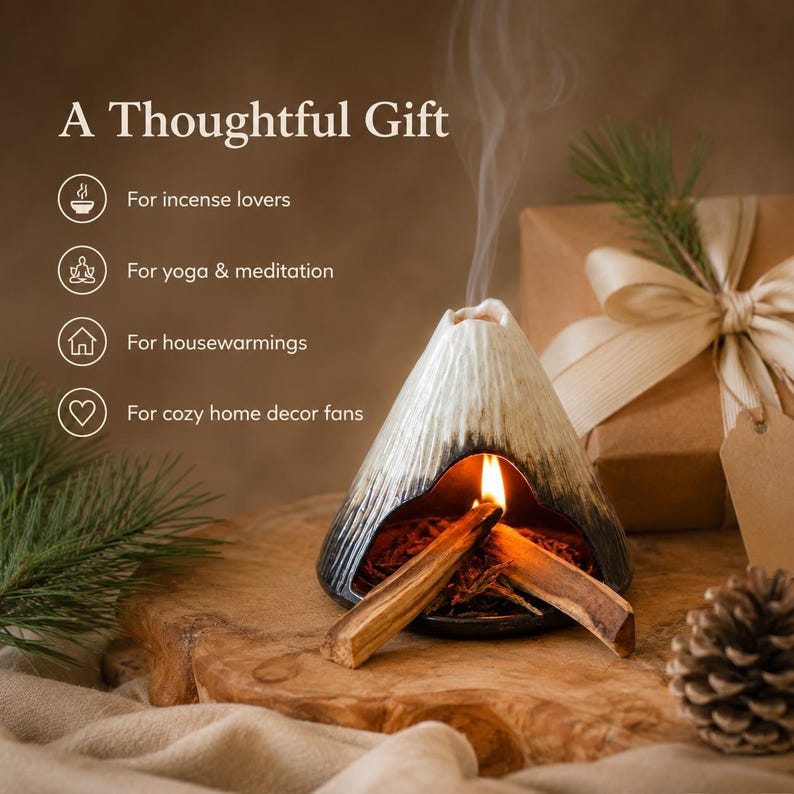 May include: A ceramic incense holder shaped like a volcano, with a lit incense stick inside, emitting smoke. The holder is black and white, with the text "A Thoughtful Gift" and other text about the product.