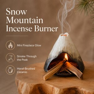 May include: A hand-brushed ceramic incense burner shaped like a snow-capped mountain. The burner has a black base and a white top, with smoke rising from the peak. The text "Snow Mountain Incense Burner" is displayed at the top.
