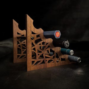 May include: A wooden wine bottle holder with a decorative cut-out design. The holder is made of dark wood and holds four bottles. The bottles are various colors, including black, blue, and gray. The background is dark.