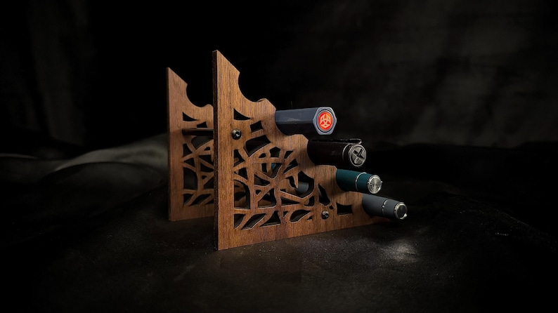 May include: A wooden wine bottle holder with a decorative cut-out design. The holder is made of dark wood and holds four bottles. The bottles are various colors, including black, blue, and gray. The background is dark.