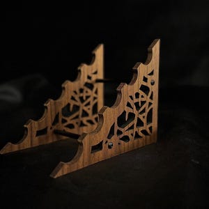 May include: A wooden display stand with a natural finish. The stand has a decorative, openwork design with a web-like pattern. The stand is approximately 6 inches wide and 4 inches tall.