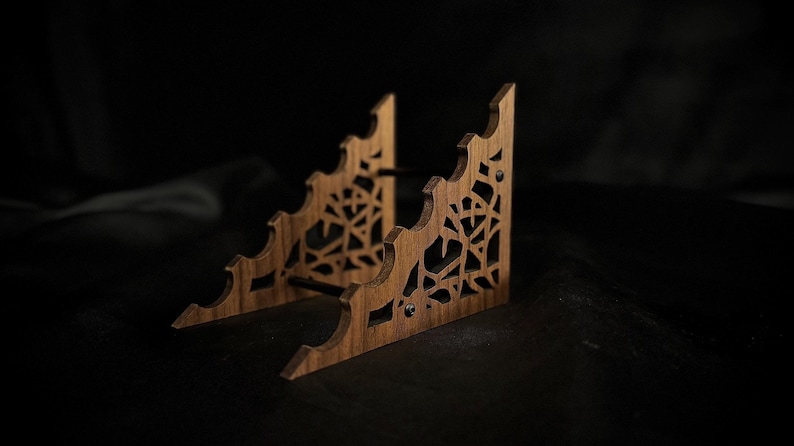 May include: A wooden display stand with a natural finish. The stand has a decorative, openwork design with a web-like pattern. The stand is approximately 6 inches wide and 4 inches tall.