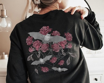 May include: Black sweatshirt with a graphic print of bats and roses. The bats are white and the roses are pink.