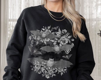 May include: Black sweatshirt featuring a grayscale floral and bat design. The design includes several bats with outstretched wings, surrounded by flowers and foliage. The sweatshirt is a crew neck style.