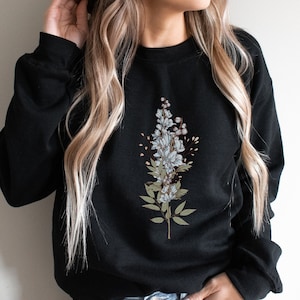May include: Black sweatshirt with a floral design featuring white and blue flowers and green leaves.