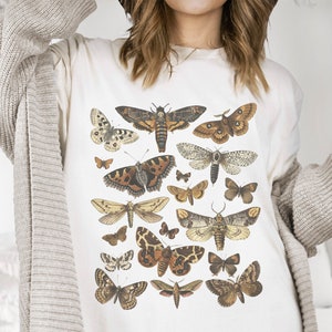 May include: White t-shirt with a vintage illustration of various butterflies and moths in shades of brown, black, and white.