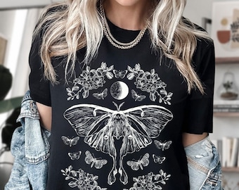 May include: Black t-shirt with a white graphic of a moth, moon, and flowers. The moth has large wings and is surrounded by small butterflies and floral designs.