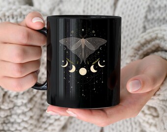 May include: Black ceramic mug with a white moth and crescent moon design. The moth has delicate wings and is surrounded by small stars and leaves. The crescent moons are in various phases.