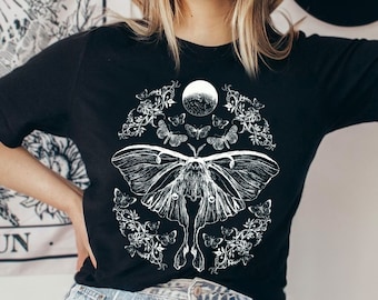 May include: Black t-shirt with a white graphic print of a moth, moon, and floral design.