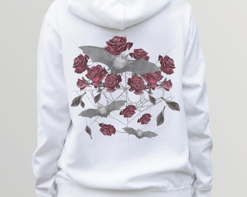May include: White hoodie featuring a detailed graphic of gray bats, deep red roses, and a spiderweb design. The artwork is centered on the back of the hoodie. The design has a gothic or alternative aesthetic.