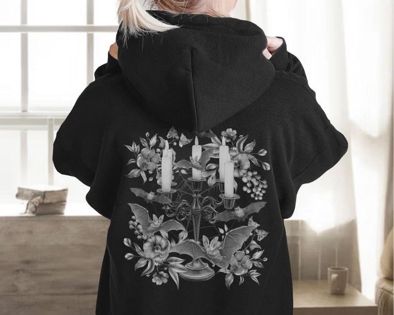 May include: Black hoodie featuring a graphic print of a candelabra with three candles, bats, and flowers in shades of grey.