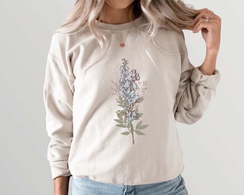 May include: A beige sweatshirt with a floral design featuring blue flowers and green leaves.