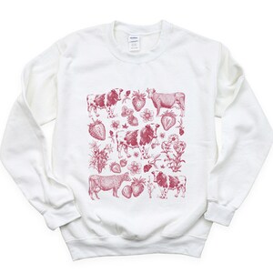 May include: White sweatshirt with a red print of cows and strawberries. The print is a repeating pattern of cows and strawberries.