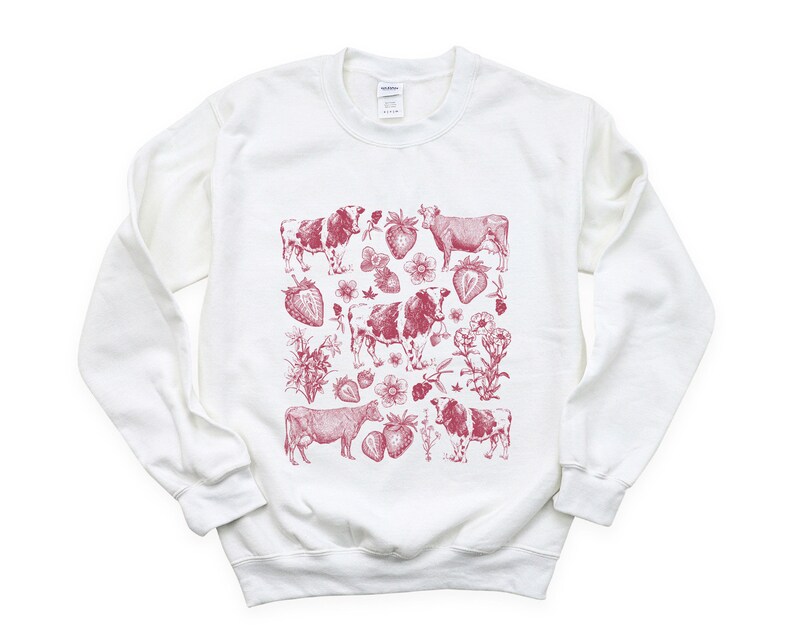 May include: White sweatshirt with a red print of cows and strawberries. The print is a repeating pattern of cows and strawberries.