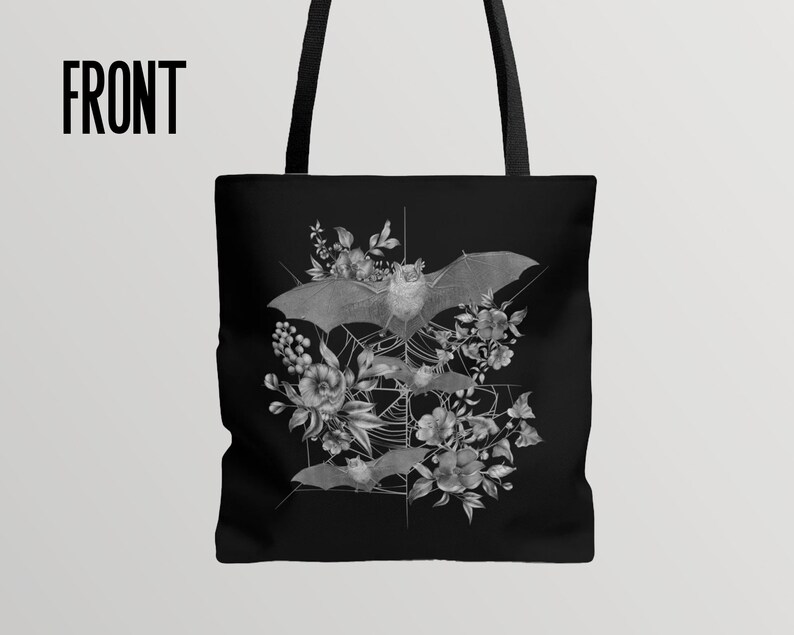 May include: Black tote bag with a white design of bats and flowers. The bats are flying in a web-like pattern with flowers surrounding them.