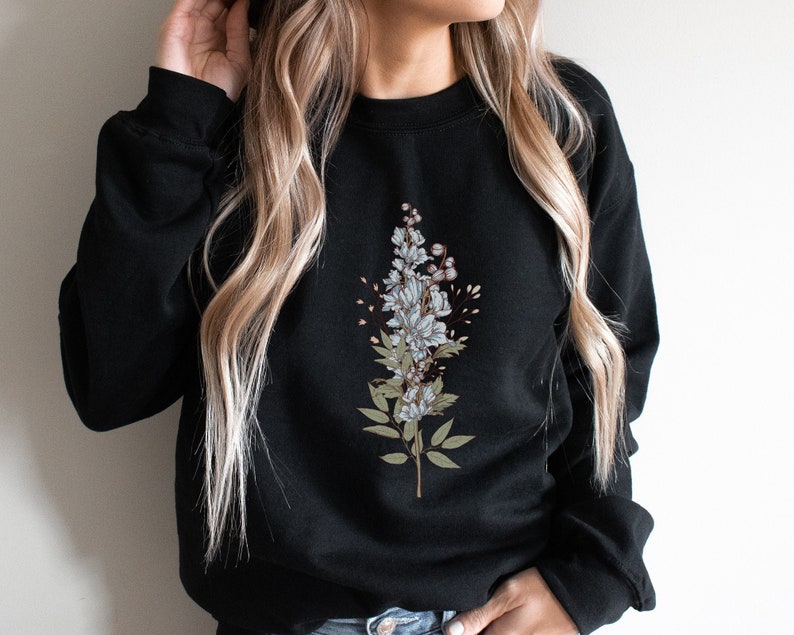 May include: Black sweatshirt with a floral design featuring white and blue flowers and green leaves.