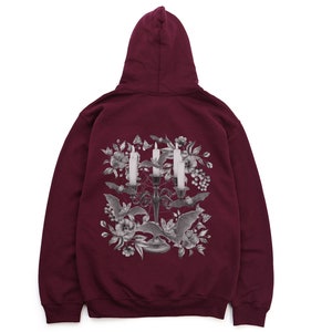 May include: Burgundy hooded sweatshirt featuring a graphic print of a candelabra with candles and bats surrounded by flowers.