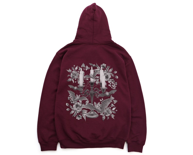 May include: Burgundy hooded sweatshirt featuring a graphic print of a candelabra with candles and bats surrounded by flowers.