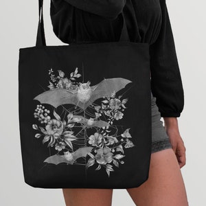 May include: Black tote bag with a white graphic design of bats and flowers. The bats are flying in a web-like pattern with flowers and leaves surrounding them.