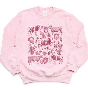 May include: Pink sweatshirt with a red graphic print of cows and strawberries.
