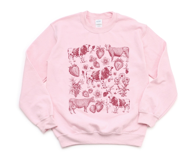 May include: Pink sweatshirt with a red graphic print of cows and strawberries.