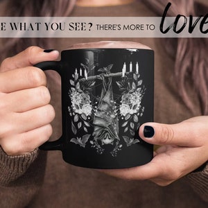 May include: Black ceramic mug featuring a white graphic of a bat hanging upside down from a branch with candles and flowers. The text "love!" is in the top right corner of the image.