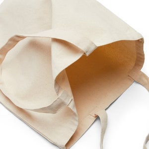 May include: A plain, off-white canvas tote bag with a single, long handle. The bag is empty and open, showing the inside of the bag.